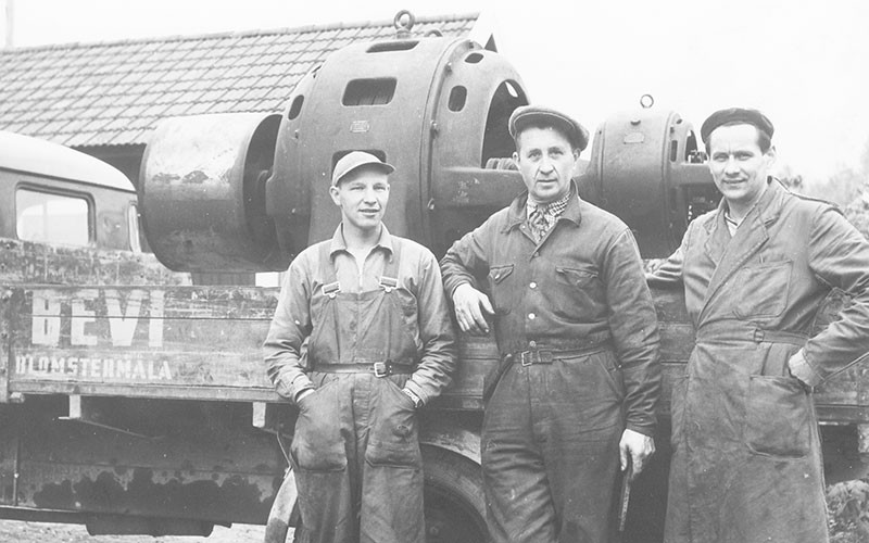 Three men in work clothes by a truck with a large electric motor on the flatbed, about 1940.