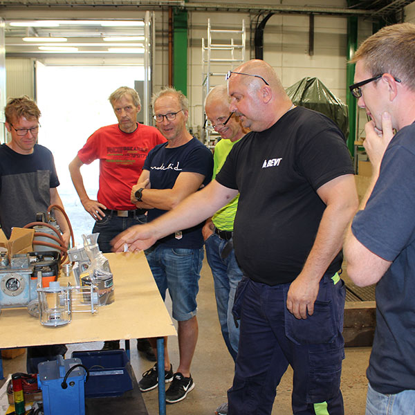 En grupp män som får utbildning om transformatorer i en verkstad.